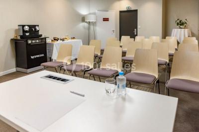 Salle lumineuse avec table en bois, chaises modernes, coin salon, lit double et murs aux tons neutres et bleu.