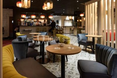 Salle lumineuse avec table en bois, chaises modernes, coin salon, lit double et murs aux tons neutres et bleu.