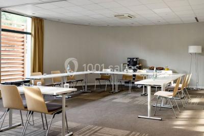 Salle lumineuse avec table en bois, chaises modernes, coin salon, lit double et murs aux tons neutres et bleu.