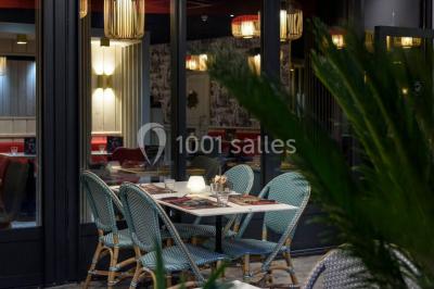 Salle lumineuse avec table en bois, chaises modernes, coin salon, lit double et murs aux tons neutres et bleu.