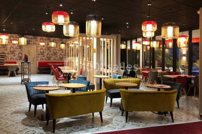 Salle lumineuse avec table en bois, chaises modernes, coin salon, lit double et murs aux tons neutres et bleu.