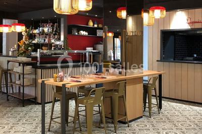 Salle lumineuse avec table en bois, chaises modernes, coin salon, lit double et murs aux tons neutres et bleu.