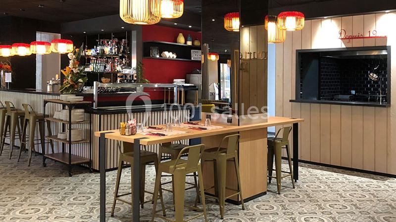 Salle de restaurant moderne avec un bar, des tables en bois, des chaises hautes et des luminaires suspendus.