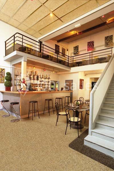 Intérieur d'un café avec un bar, des tables et chaises, un escalier et une mezzanine aménagée.