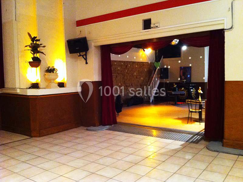 Salle avec carrelage clair, rideaux rouges ouverts donnant sur un espace avec scène, chaises et éclairage tamisé.