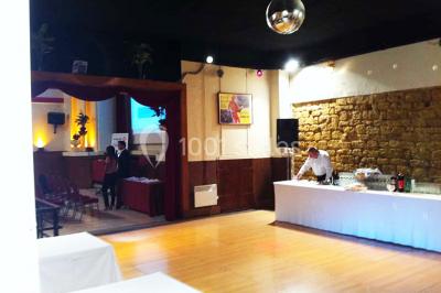 Salle avec mezzanine, tables et chaises jaunes, projection d'un match de rugby sur un mur, éclairage chaleureux.