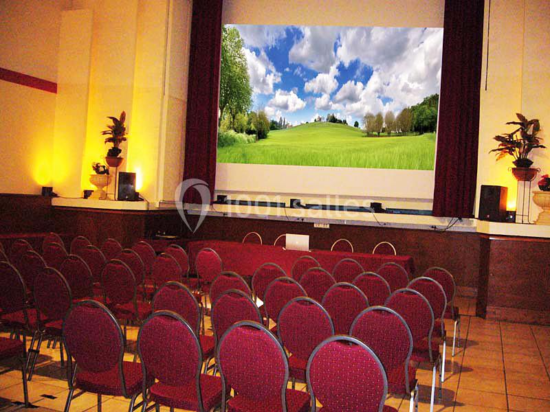 Salle de projection avec des rangées de chaises rouges face à un écran affichant un paysage champêtre.