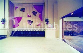 Salle avec un mur décoré de rideaux violets et de motifs papillons, rangée de chaises noires au fond.