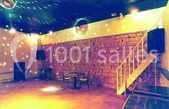 Salle avec mezzanine, tables et chaises jaunes, projection d'un match de rugby sur un mur, éclairage chaleureux.