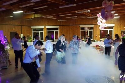 Des personnes dansent et discutent dans une salle décorée, avec un sol enfumé et des lumières colorées.