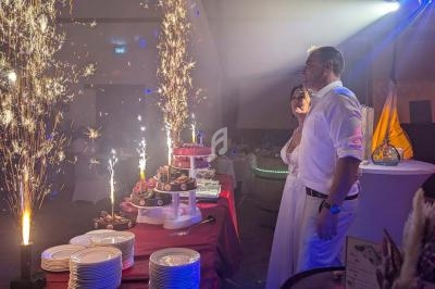 Un couple en tenue de mariage observe une table de desserts illuminée par des fontaines de feu dans une salle festive.