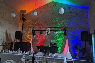 Salle décorée pour un événement avec éclairage coloré, tables dressées et équipement de sonorisation sur scène.
