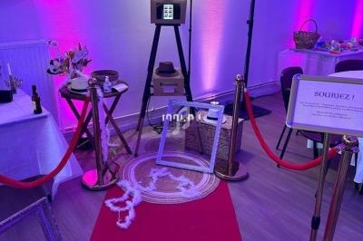 Cabine photo avec accessoires sur un tapis rouge, entourée de cordons dorés et éclairée par une lumière violette.