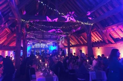 Salle de réception illuminée de lumières colorées, avec des invités assis à des tables décorées pour un événement festif.