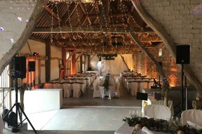 Salle de réception rustique décorée avec des guirlandes lumineuses, des tables dressées et des murs en pierre apparente.