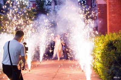 Un couple marche sous des gerbes d'étincelles lors d'une cérémonie, photographié par un professionnel.
