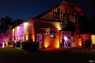Façade d'une grande maison à colombages éclairée par des lumières colorées en soirée, avec des personnes à l'entrée.