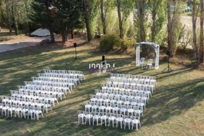 Chaises blanches alignées en extérieur devant une arche décorative, entourées d'arbres et de verdure.