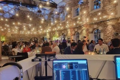 Salle en pierre illuminée par des guirlandes, remplie de convives attablés, vue depuis une table de mixage DJ.