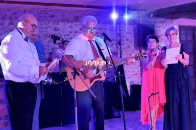 Un homme joue de la guitare sur scène entouré de personnes chantant dans un cadre intérieur éclairé en violet.