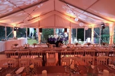 Intérieur d'une tente de réception décorée avec des tables dressées, des chaises blanches et un éclairage chaleureux.