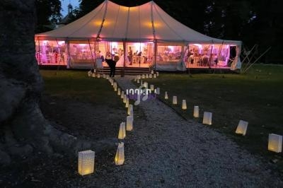 Chemin éclairé par des lanternes menant à une tente lumineuse installée dans un jardin en soirée.