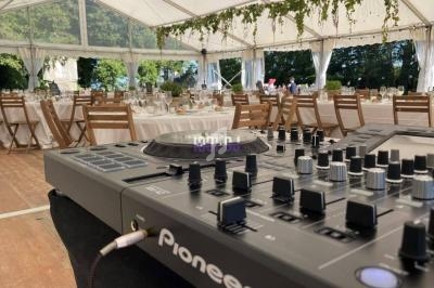 Table de mixage en premier plan dans une tente décorée pour un événement avec des tables dressées en arrière-plan.