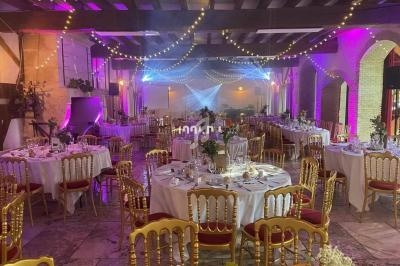 Salle de réception décorée avec des tables rondes dressées, des chaises dorées et des guirlandes lumineuses suspendues.