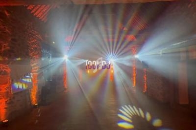 Effets lumineux colorés projetés dans une salle en pierre avec des murs éclairés en orange et un logo lumineux au fond.