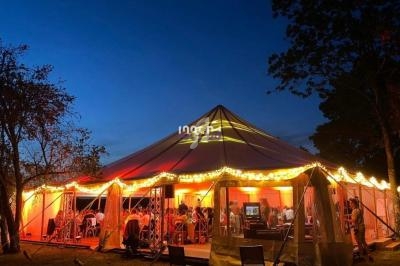 Tente éclairée en soirée, abritant des convives assis, entourée d'arbres sous un ciel crépusculaire.