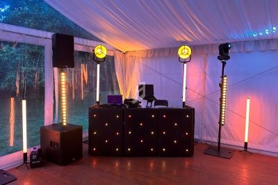 Installation de DJ sous une tente avec éclairage coloré, comprenant une table, des enceintes et des lumières LED.