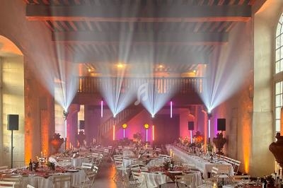 Salle de réception illuminée avec des projecteurs colorés, tables dressées et ambiance festive.