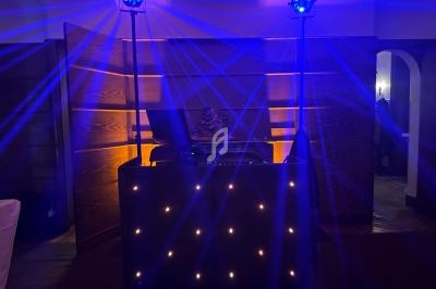 Installation de DJ avec lumières bleues et projecteurs sur pied dans une salle sombre au décor en bois.