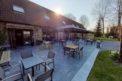 Terrasse extérieure d'un restaurant avec des tables et chaises sur un sol en pierre, entourée de verdure et arbres.