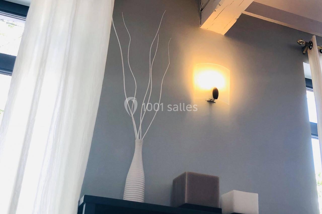 Vase blanc avec branches décoratives posé sur un meuble noir, éclairé par une applique murale sur fond de mur gris.