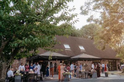 Terrasse extérieure d'un restaurant avec des tables et chaises sur un sol en pierre, entourée de verdure et arbres.