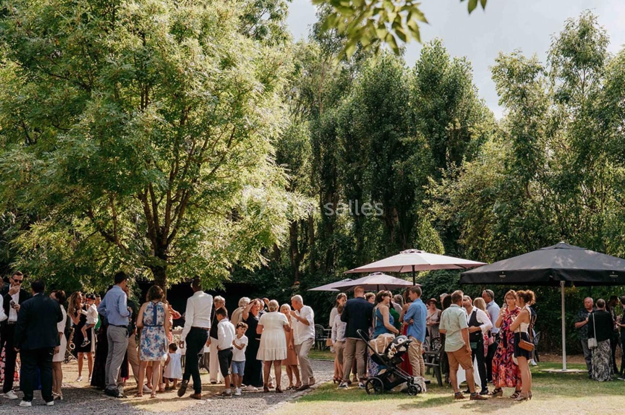 Groupe de personnes rassemblées en extérieur sous des arbres, avec des parasols et une ambiance conviviale.