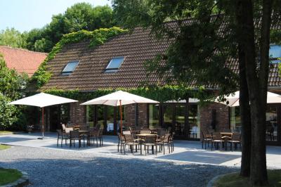 Terrasse extérieure d'un restaurant avec des tables et chaises sur un sol en pierre, entourée de verdure et arbres.