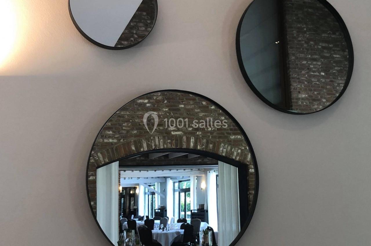 Trois miroirs ronds accrochés sur un mur beige, reflétant une salle lumineuse avec des tables dressées.