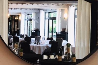 Terrasse extérieure d'un restaurant avec des tables et chaises sur un sol en pierre, entourée de verdure et arbres.