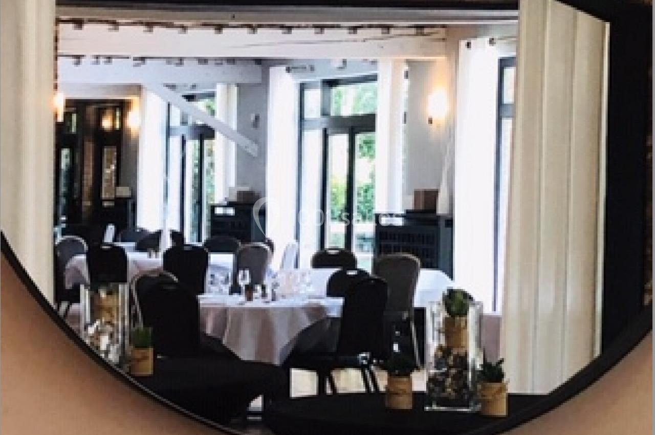 Reflet d'une salle de restaurant élégante avec tables dressées, vu à travers un miroir rond encadré de noir.
