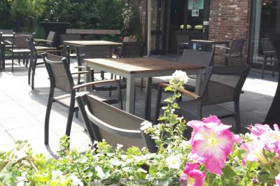 Terrasse extérieure d'un restaurant avec des tables et chaises sur un sol en pierre, entourée de verdure et arbres.