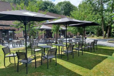 Terrasse extérieure d'un restaurant avec des tables et chaises sur un sol en pierre, entourée de verdure et arbres.