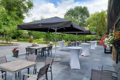Terrasse extérieure d'un restaurant avec des tables et chaises sur un sol en pierre, entourée de verdure et arbres.