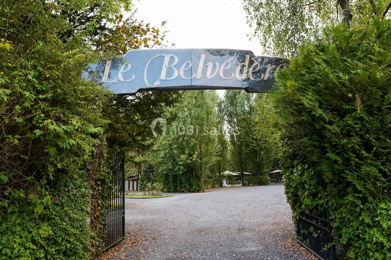 Entrée d'un lieu nommé ’Le Belvédère’, avec une arche métallique entourée de verdure et un chemin menant à l'intérieur.