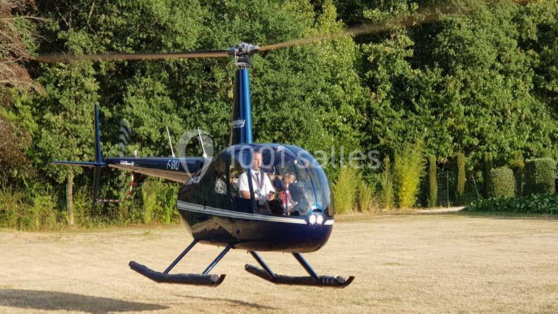 Un hélicoptère bleu en vol stationnaire au-dessus d'une pelouse, avec des arbres en arrière-plan.