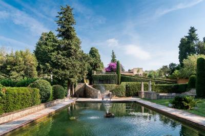 Jardin éclairé de nuit avec piscine, terrasse en pavés et bâtiments entourés de végétation.