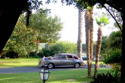 Groupe de personnes rassemblées dans une cour extérieure verdoyante devant un bâtiment en pierre avec des volets bleus.