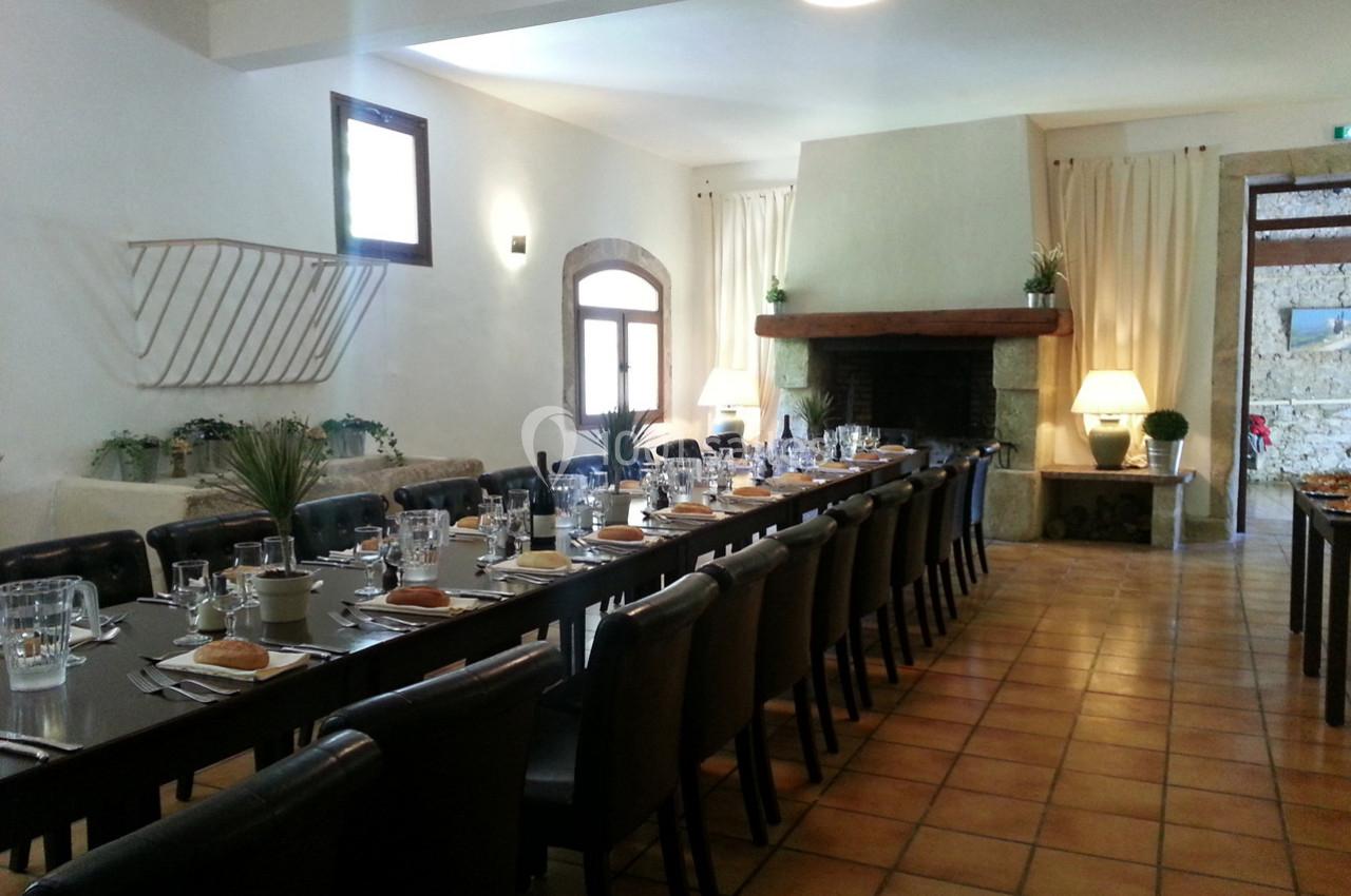 Salle à manger lumineuse avec de longues tables dressées, chaises noires, cheminée et décoration sobre.