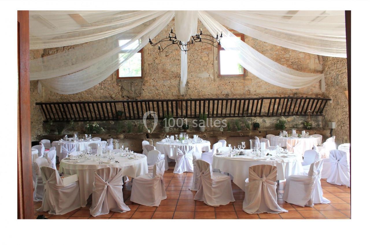 Salle de réception décorée avec des tables rondes nappées de blanc, des chaises assorties et un plafond drapé.